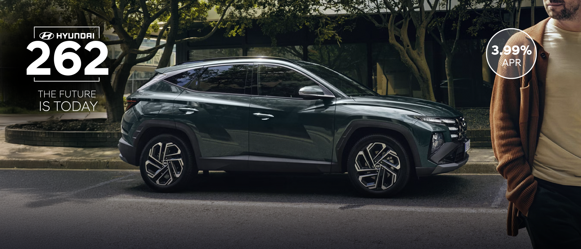 A man walking near a Hyundai&nbsp;TUCSON Hybrid parked by some trees.